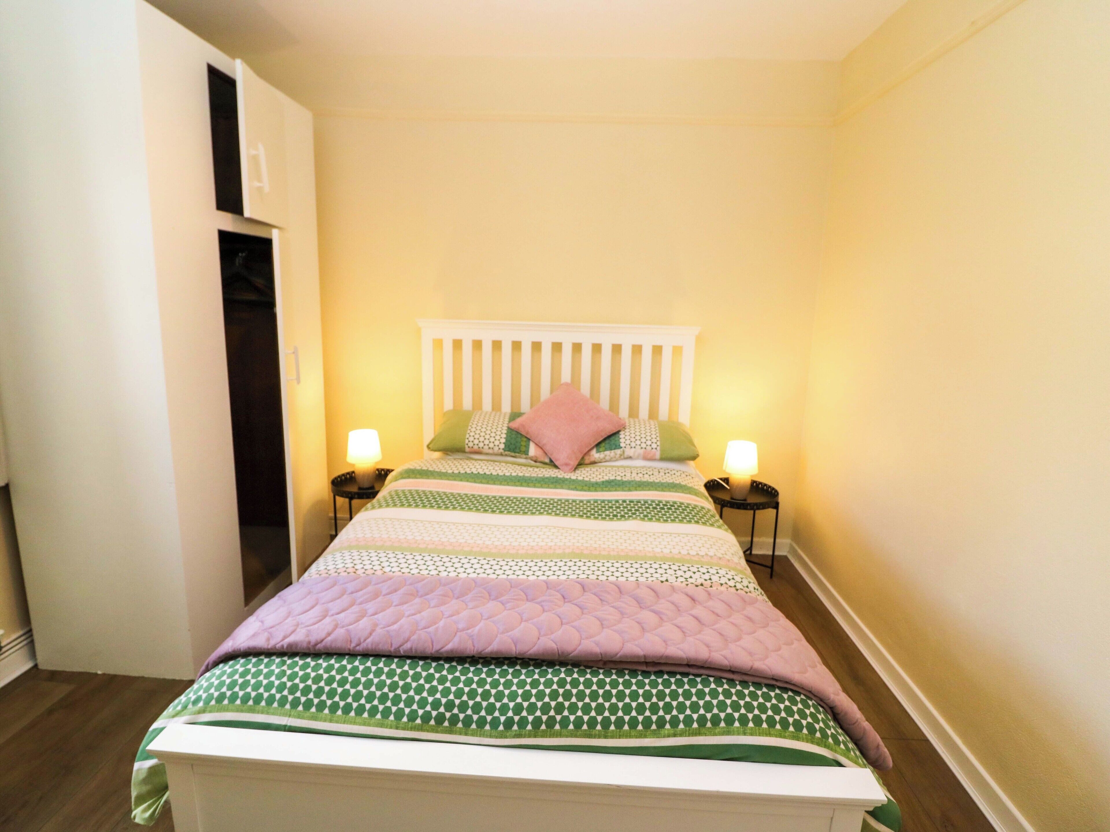 Un dormitorio con cama, dos mesitas de noche y una puerta.