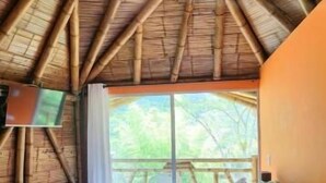 A room with a thatched roof, a bed with white bedding, and a wooden desk. - Hotel y termales Las Heliconias (Zetaquira)