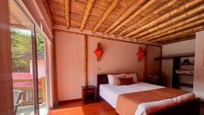 A bedroom with a large bed, a nightstand, a wooden ceiling, and a sliding glass door leading to an outdoor area. - Hotel y termales Las Heliconias (Zetaquira)