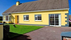 Ein gelbes Gebäude mit einem braunen Dach, großen Fenstern und einem kleinen Garten.