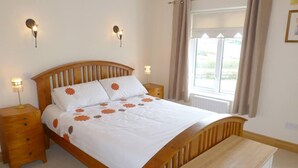 A bedroom with a wooden bed, bedside lamps, a window with curtains, and a bedside table.
