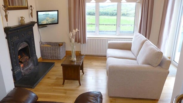 A living room with a fireplace, a sofa, a television, and a view of the outdoors.