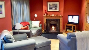 A living room with a fireplace, a television, and a sofa. - 4 Bed in Dunquin (oc-ii08697) (Dunquin)