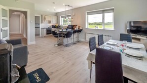 Une cuisine moderne avec des tabourets de bar, un coin repas avec une table dressée pour deux personnes, et un téléviseur dans le salon.