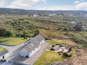 A large, white building with a tiled roof, surrounded by a well-maintained lawn and a small garden area with various plants and a seating area. - 3 Bed in Cashel (oc-a32863) (Glynsk Cottages)