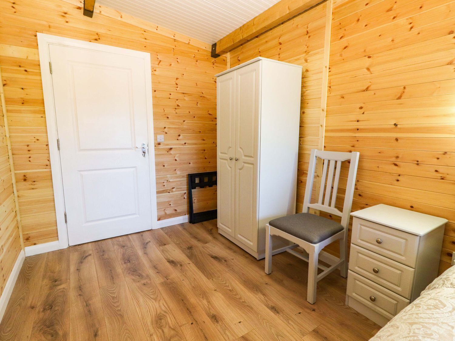 Ein Zimmer mit Holzwänden, einem weißen Kleiderschrank, einem Stuhl, einem Nachttisch und einem Bett.