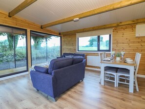 A modern, open-plan living and dining area with a wooden ceiling, large windows, and a grey sofa.