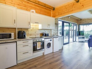 A modern kitchen with wooden walls, white cabinets, a microwave, a coffee maker, a sink, a stove, and a washing machine.