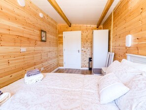 A wooden-paneled room with a bed, a chair, a wardrobe, and a door.