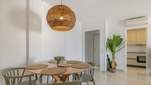 A dining area with a round table, six chairs, a woven pendant light, and a potted plant. - Apartment 'Las Conchas' with Sea View, Wi-Fi and Air Conditioning (Cunit)