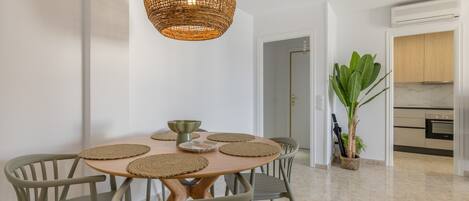 A dining area with a round table, six chairs, a woven pendant light, and a potted plant.