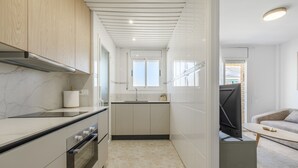 A modern kitchen with a built-in oven, a window, and a TV on a stand. - Apartment 'Las Conchas' with Sea View, Wi-Fi and Air Conditioning (Cunit)