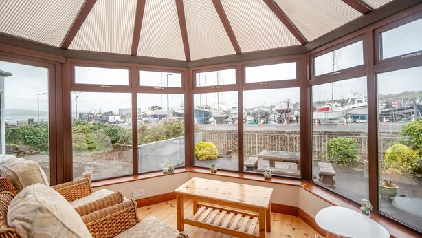 A conservatory with a view of a marina, wicker furniture, and a wooden table. - 3 Bed in Dingle (oc-ii05995) (Dingle)