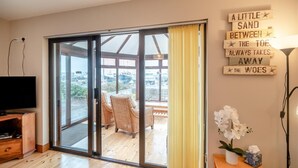 A room with a sliding glass door leading to an outdoor area, wicker chairs, a flat-screen TV, and a wall with a motivational quote. - 3 Bed in Dingle (oc-ii05995) (Dingle)