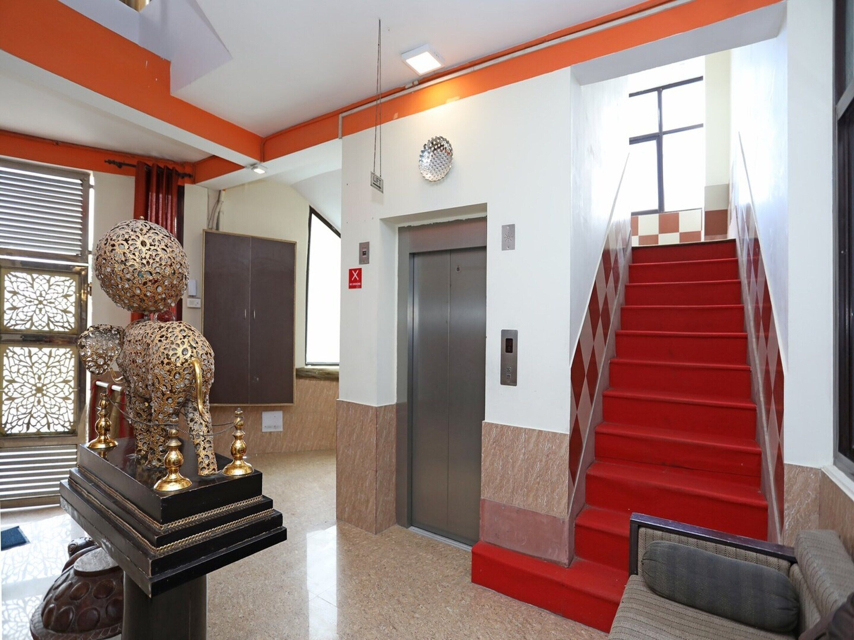 A lobby with a red carpeted staircase, a decorative elephant sculpture, and an elevator.
