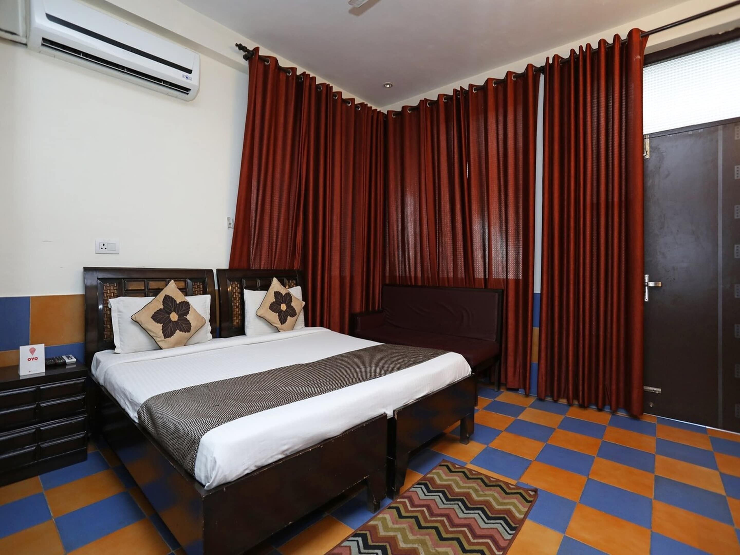 A hotel room with a bed, a desk with drawers, an air conditioning unit, a door, and a check-in counter.