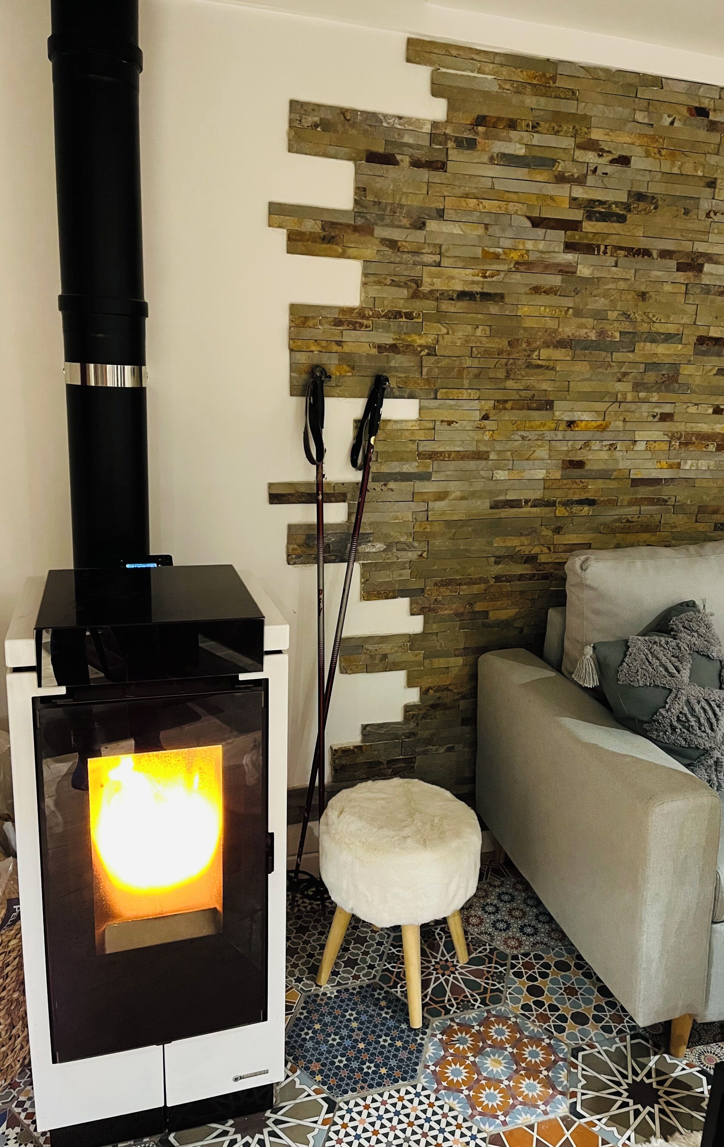 A room with a wood-burning stove, a sofa, and a patterned floor.