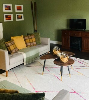 Un salon avec un canapé, deux tables basses, une cheminée et des tableaux encadrés accrochés au mur.