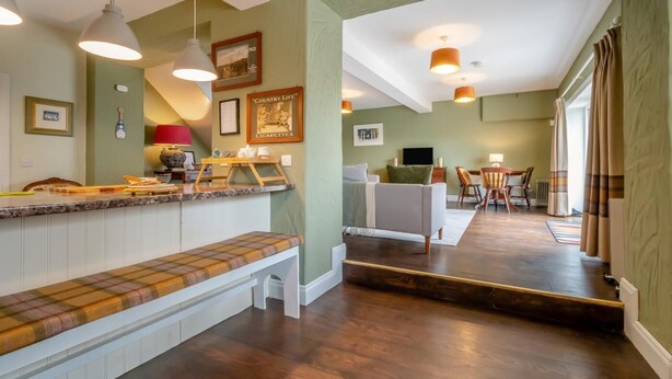 Una cocina moderna con una banca integrada, un comedor con mesa y sillas, y una sala de estar con sofá y televisor.