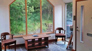 Une pièce dotée d’une grande fenêtre, d’un banc en bois, de deux chaises et d’un luminaire fixé au plafond.