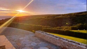Une vue sur le coucher de soleil depuis un patio en pierre avec un mur de briques, donnant sur un paysage vallonné.