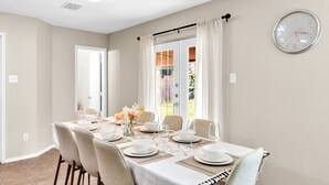 Un comedor con una mesa dispuesta para seis personas, un reloj en la pared y vistas a través de una ventana.