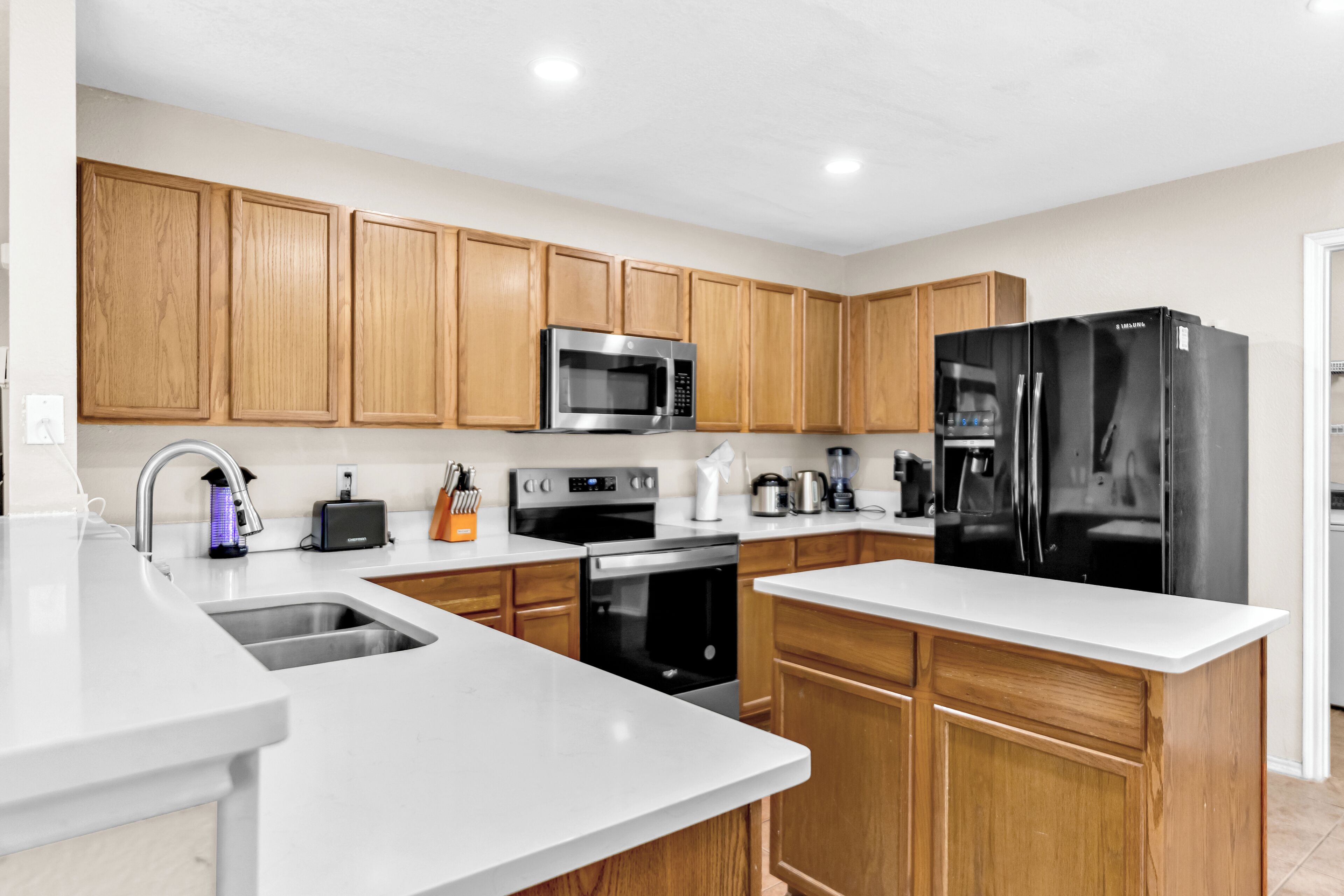 A modern kitchen with wooden cabinets, stainless steel appliances, and a white countertop.