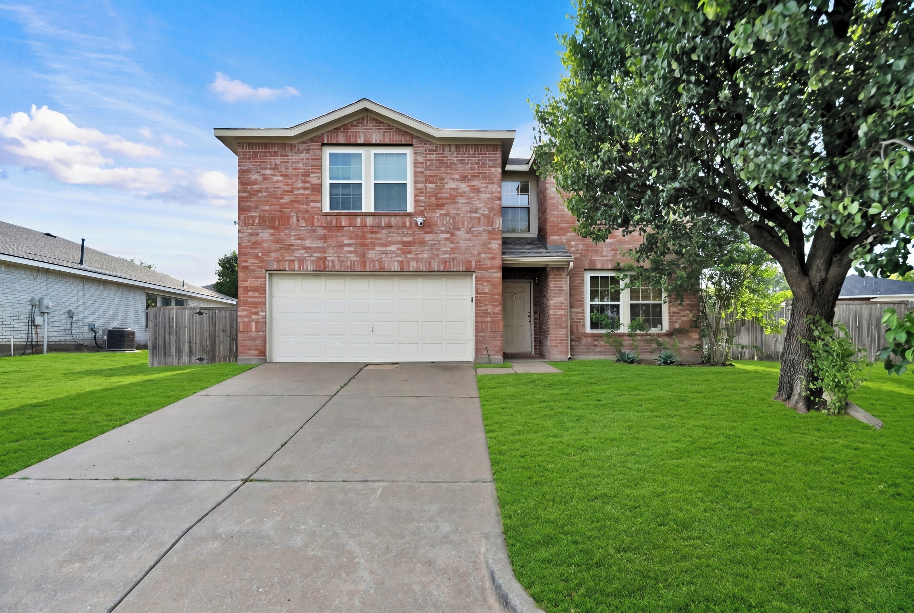 A two-story house with a garage, a well-maintained lawn, and a large tree.