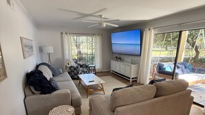Ein geräumiges Wohnzimmer mit Deckenventilator, Fernseher und Blick ins Freie.