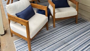 Eine überdachte Terrasse mit Holzmöbeln, einem gemusterten Teppich und einem dekorativen Wandelement.