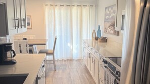 Eine moderne Küche mit Essbereich, Holzboden und Blick durch ein mit Vorhängen drapiertes Fenster.