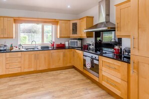 A modern kitchen with wooden cabinets, a stainless steel range hood, a microwave, and a stove. - 3 Bed in Moville (oc-ii07029) (Moville)