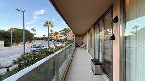 Un balcon donnant sur une route, des palmiers et un bâtiment en arrière-plan.