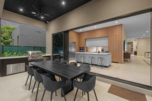 Une cuisine extérieure avec un espace repas, un bar et une vue sur la maison.