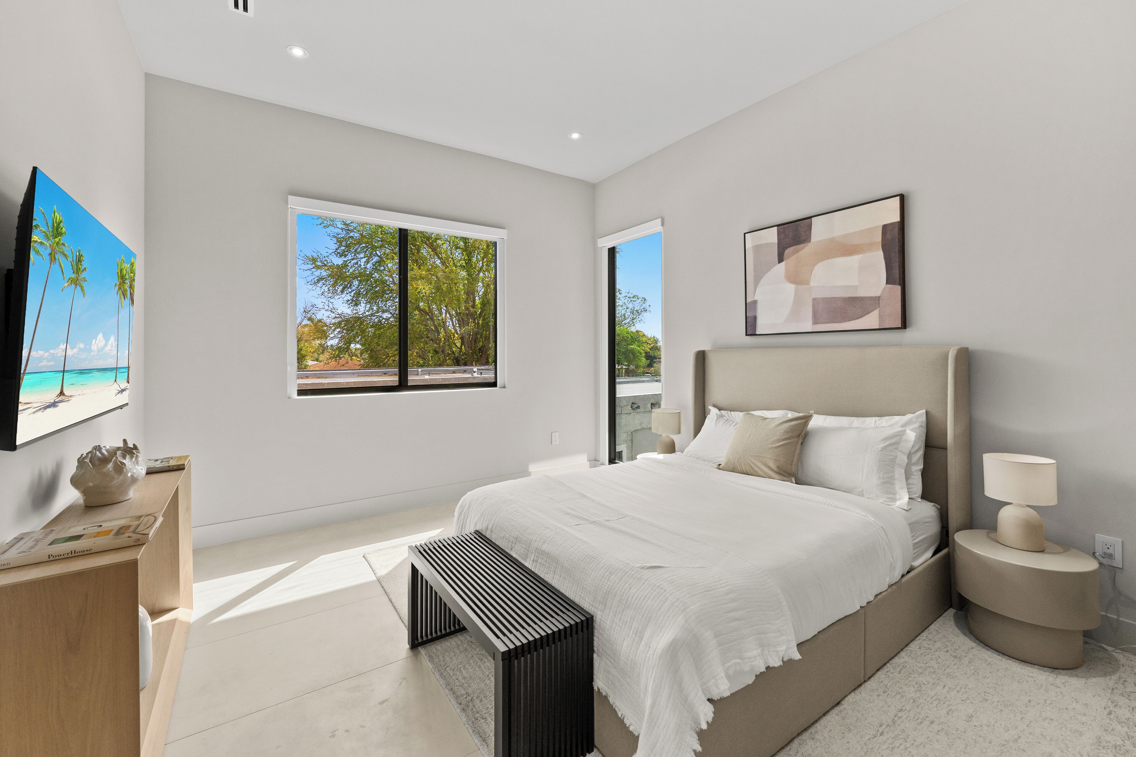 Une chambre à coucher moderne avec un grand lit, des tables de chevet, un banc et des œuvres d’art accrochées aux murs.