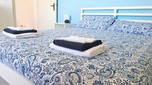 Un lit bien fait, recouvert d’une couvre-lit à motifs bleus et blancs, avec une tête de lit blanche et des oreillers assortis.