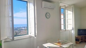 Une pièce dotée d’une grande fenêtre, d’un climatiseur, d’une table recouverte d’une cloche en verre et d’une horloge murale.