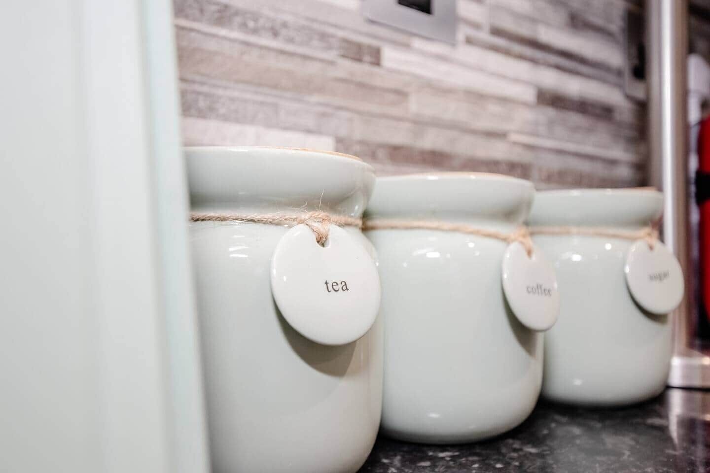A row of white ceramic containers with tags labeled 'tea,' 'coffee,' and 'tea.'