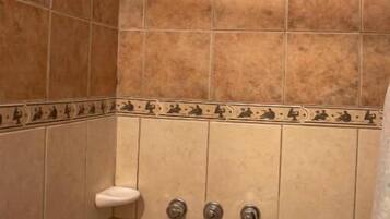 Ducha con azulejos color beige, un jabonera blanca y un cabezal de ducha.
