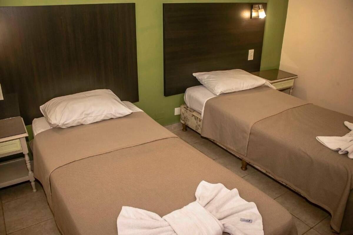 Une chambre d’hôtel avec deux lits, chacun étant équipé d’un oreiller et d’une couverture. Une table de chevet avec une lampe se trouve sur le côté gauche.