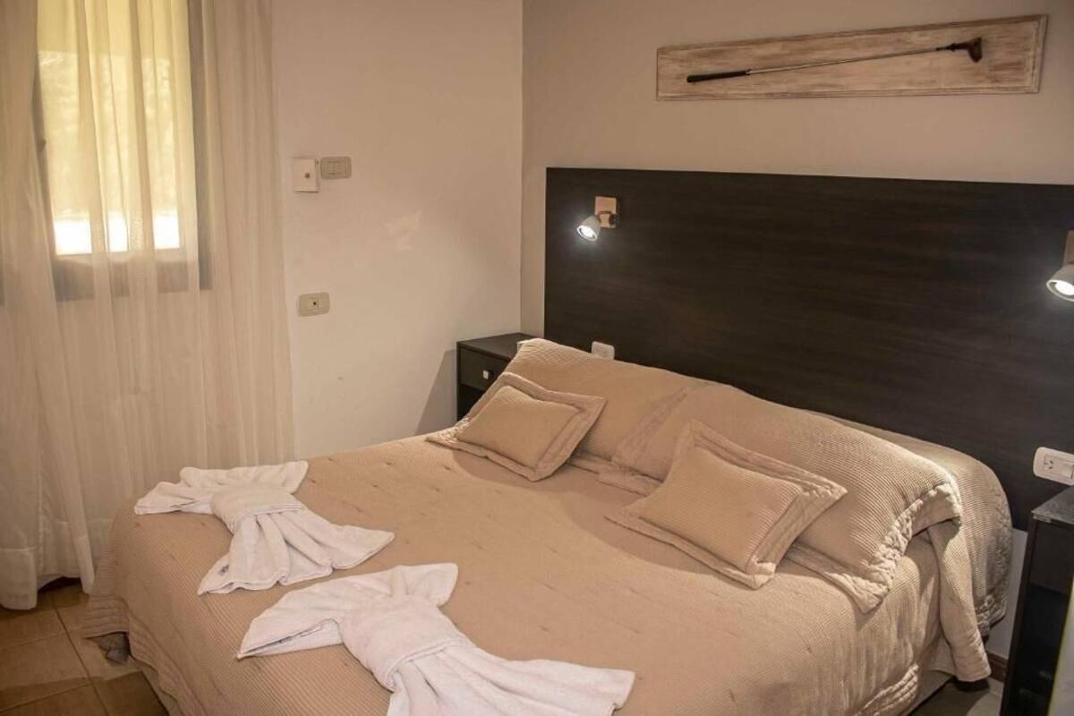 Une chambre à coucher comprenant un lit, des tables de chevet, une tête de lit et un luminaire fixé au mur.