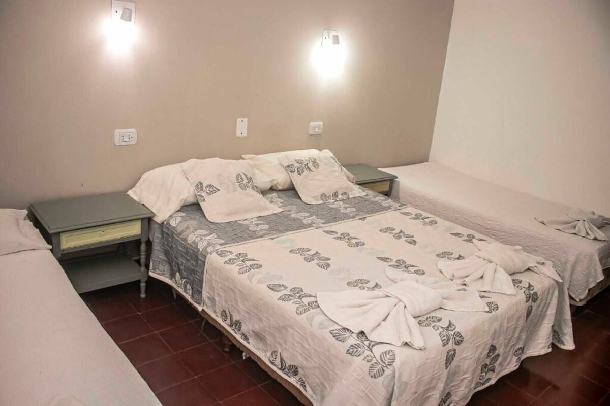 Une chambre avec deux lits, chacun recouvert d’une couvre-lit à motifs floraux, une table de chevet et un luminaire fixé au mur.