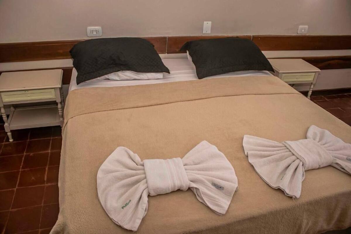 Une chambre d’hôtel avec un lit double, deux tables de chevet, un banc et des serviettes disposées sur le lit.