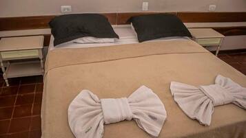 A hotel room with a double bed, two bedside tables, a bench, and towels arranged on the bed.
