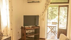 A living room with a sofa, a TV on a wooden stand, a desk with drawers, and a sliding glass door leading to an outdoor area.