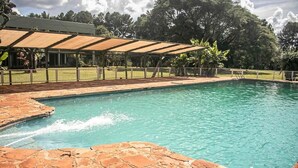 A swimming pool with a stone deck, a covered seating area, and a grassy area with trees in the background.