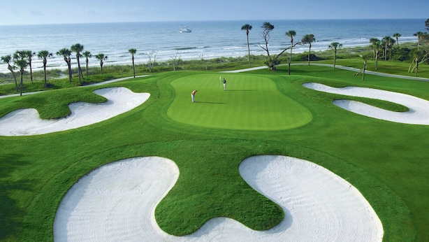 Un parcours de golf avec des bunkers de sable, une personne jouant au golf et une vue sur l’océan.