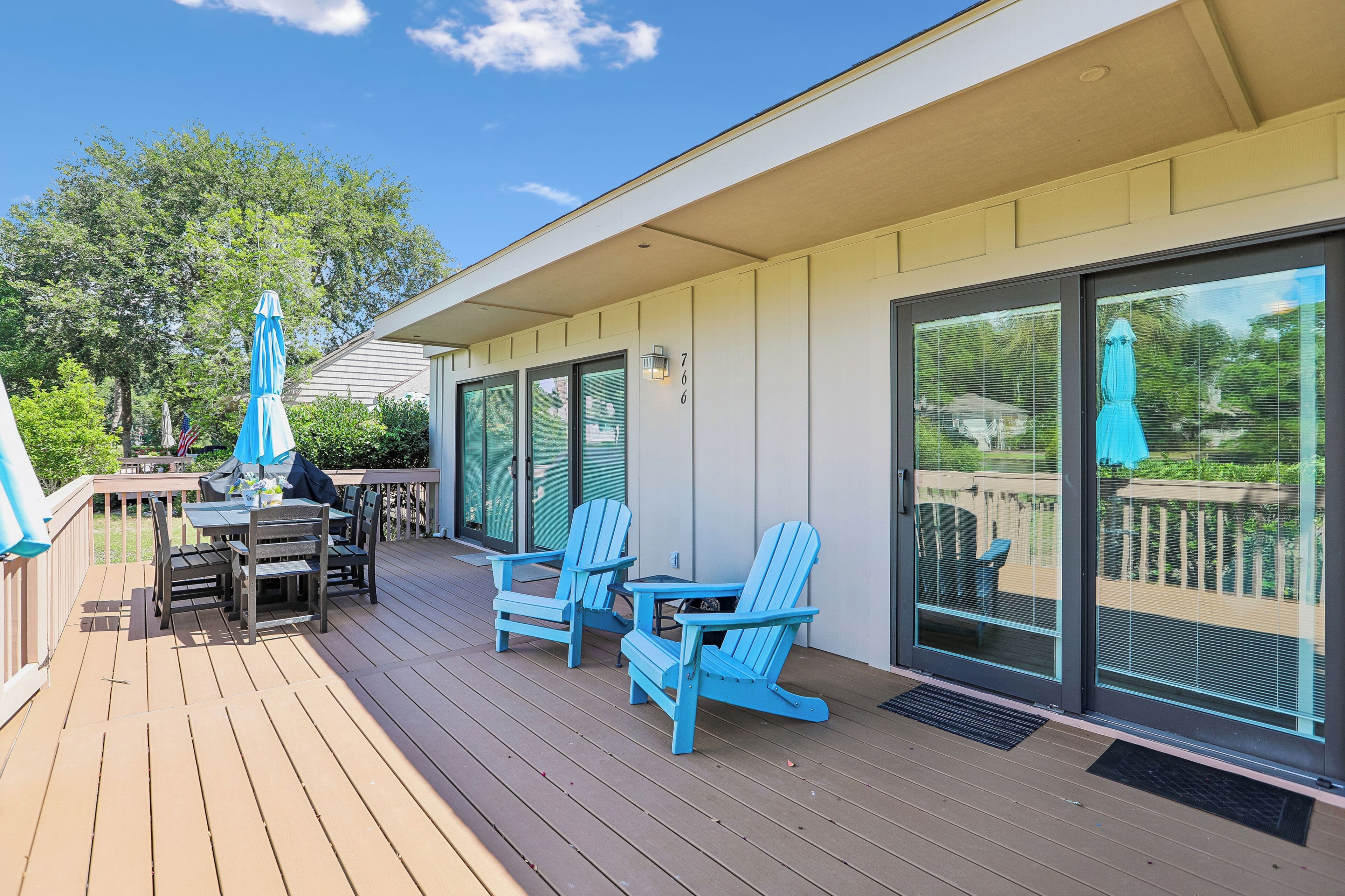 An outdoor deck with a table and chairs, a covered patio area with umbrellas, and a view through large sliding glass doors.