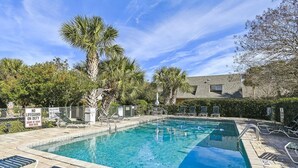 Une piscine avec des chaises longues, des palmiers et un bâtiment en arrière-plan.