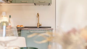 Une cuisine avec un robinet doré, un saladier rempli d’oranges et une bouteille de vin.